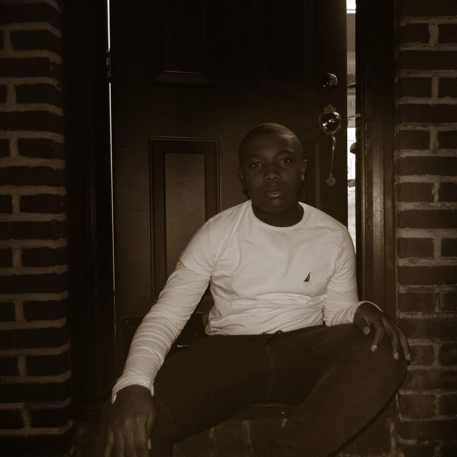 A sepia-toned self-portrait of me; I’m sitting down in front of a door.